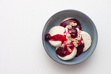 Cottage cheese pancakes or fritters with cherry sauce and chopped nuts on plain white background. Isolated. Healthy breakfast.