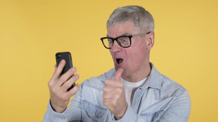 Excited Casual Old Man Celebrating Success on Smartphone, Yellow Background