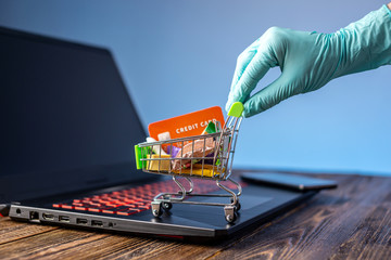 Hand in a sterile glove holds a shopping cart with a credit card. Internet purchasing during the...