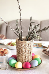 Wicker vase with willow and colored eggs on table for Easter