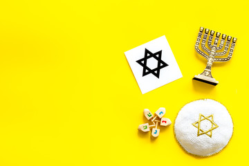 Jewish Kippah Yarmulkes hats, star of David and menorah on yellow table. Top view, copy space