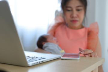 Fototapeta premium mother playing mobile phone in business home office with cute baby newborn sleeping