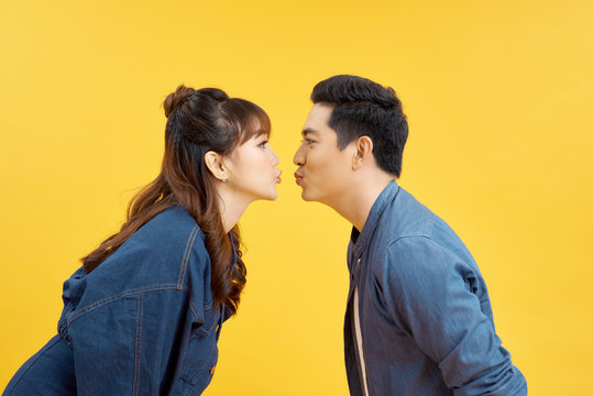 Profiles of girlfriend and boyfriend giving each other an air kiss over yellow