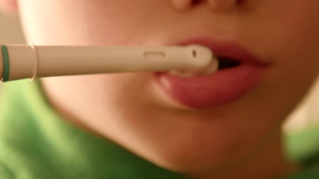 A Kid Brushes his theeth with an electric toothbrush