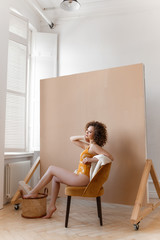 Fun funny playful attractive cheerful girl with afrocudry in a bright yellow bodysuit and sweater laughing posing for the camera enjoying herself on a beige background, fashion shooting