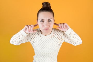 The young woman covers her ears tightly with her fingers and looks angrily