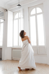 Beautiful sweet cheerful tender happy natural sleepy girl with Afro curls wrapped in a blanket wakes up and enjoys the morning looks out the window against the background of large vintage Windows