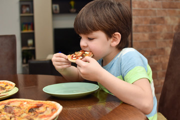 Happy boy eats pizza. Child eating pizza, ordering fast food for dinner