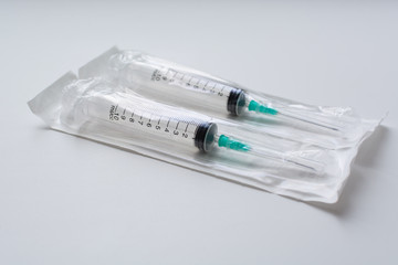 Close-up view of 2 disposable medical syringes in a package on a uniform light gray background, the...