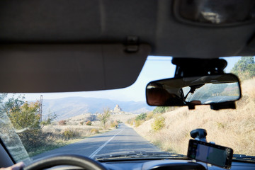 View from inside car window to the road and autumn mountain landscape. Asphalt road in perspective in a sunny day