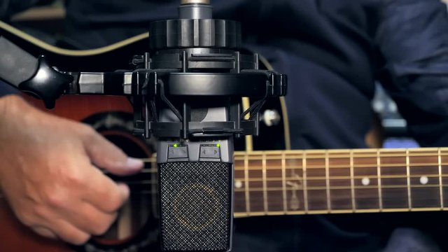 Closeup of a big diaphragm condenser mic on a recording session of an acoustic guitar. Mic is on focus while guitarist hands and acoustic guitar are out of focus