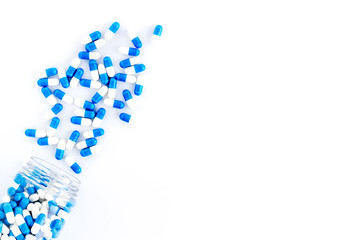 Blue and white capsules poured from a bottle - sports supplement creatine - on white background top view copy space