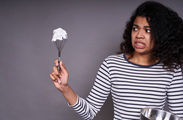 Tired young dark-skinned lady makes cream for cake.