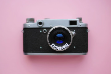 Old Retro film photo camera and the word Smile on a pink background. Top view, tender minimal flat lay style composition. Summer concept.