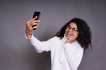 Fototapeta premium Beautiful dark-skinned girl takes a selfie on a gray background.