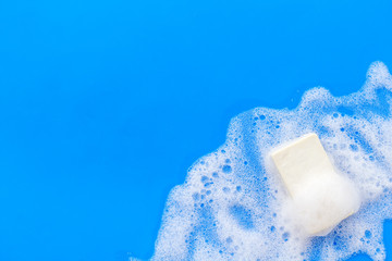 Soap bar with foam on blue background top-down copy space