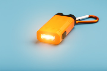An orange led flashlight with a carabiner glows on a blue background.
