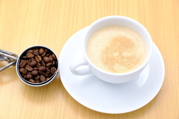 Coffee cup and beans on wooden kitchen table. Top view with morning sunlight
