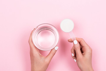 Woman hands with a scoop with collagen or protein powder and a glass of water. Trendy beauty...