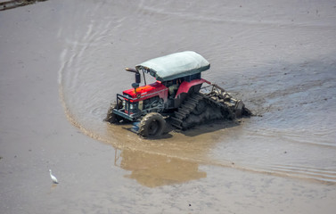A tractor is doing its job early Mac during the hot season in a paddy field fills with water and mud. 