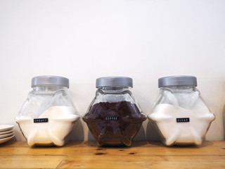Close up glass bottles of cream; coffee and sugar powder with name tag label on wooden table