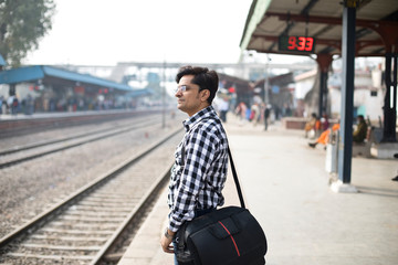 Man with holding bag waiting at railroad station platform