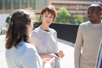 Group of serious people standing on street and talking. Concentrated friends discussing some...