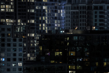 Fototapeta na wymiar Windows of a big city apartment building at night. Lights are lit in the homes and rooms. Multi storey offices and apartments, people at home late night.
