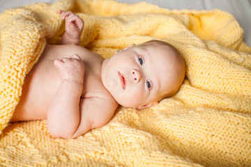 .Cute infant baby looking at camera in a knitted yellow plaid on a white bed. Copyspace