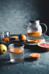 Citrus tea in a transparent teapot on a dark concrete background. Healthy drink, vegan, eco product.