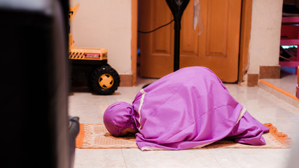 Fototapeta na wymiar Little Asian Muslim girl in purple muslimah clothes is praying at home. The concept of worshiping or praying at home to avoid the spread of the coronavirus or COVID-19 pandemic. Ramadan illustration.