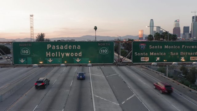 Los Angeles. Downtown. 2019. Aerial view of the green road information sign above the highway 110. Sunset time. The freeway is busy with traffic. A group of skyscrapers is seen ahead. 4K