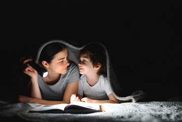 Happy family. Time for stories. Delighted happy cute mother and son enjoying a book before sleeping and using a flashlight.