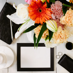 Flat lay styled framed composition with blank frame, sunglasses, saturated bouquet, black leather notebook and parfume on wooden desk