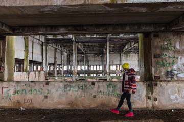 Naklejka na ściany i meble young women in bright jacket and red shoes walking in old abandoned cloth factory ruins in Kargaly village, near Almaty, Kazakhstan