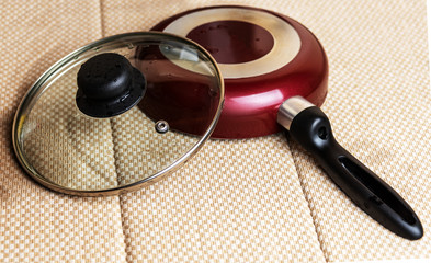 A frying pan with a glass lid dries after washing on a napkin.