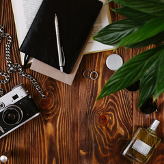 Masculine personality concept with vintage film camera, decorative chain, black leather notebook and parfume on wooden desk. Elegant modern template for men branding identity. Framed composition