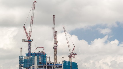 Working crane on a modern office building under construction against cloudy sky in Singapore timelapse.