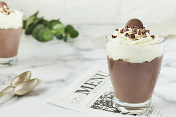 Chocolate mousse and cream cup for a restaurant menu with spoons on white marble background.