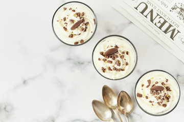 Flat lay of chocolate mousse and cream cup for a restaurant menu with spoons on white marble background.