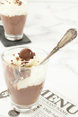 Chocolate mousse and cream cup half empty on white marble background.