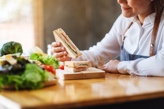 Closeup image of a female chef cooking and eating a whole wheat sandwich in kitchen