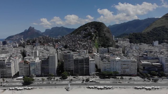 Aerial sideways pan of near empty Copacabana beach and boulevard in Rio de Janeiro during the COVID-19 Corona virus outbreak with luxury apartment buildings in front and large favela shantytown behind