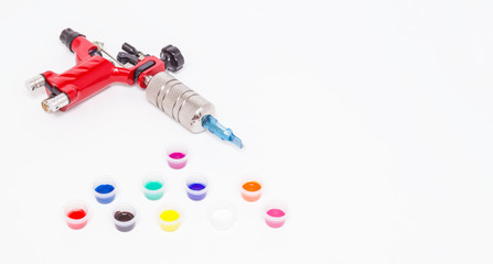 Rotary tattoo machine and color paints in disposable plastic jars on a white background. Free space for text. Side view.