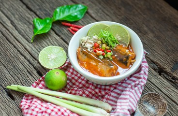 Sardines in tomato sauce with lemongrass, kaffir lime leaves, chilies, lime on wooden table.