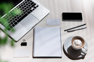 Gadgets, coffee, work tools on a white table indoors. Creative, cozy workplace at home office, inspirational mock up with plant shadows on surface. Concept of remote office, freelance, atmosphere.
