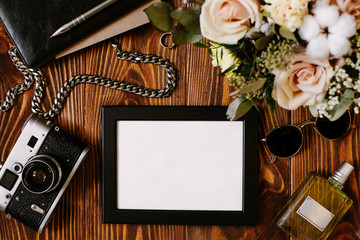 Obraz premium Men temper concept with blank frame, vintage film camera, decorative chain, black leather notebook and parfume on wooden desk. Elegant modern template for men branding identity. Framed composition