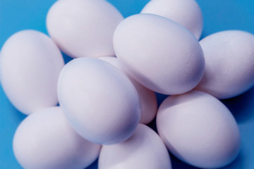 Eggs of a white hen are laid on a blue background. Eggs are shown in close-up, they are whole, raw