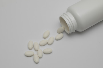 White round tablets covered with a cover are scattered from a plastic can with them. Drugs, pill.