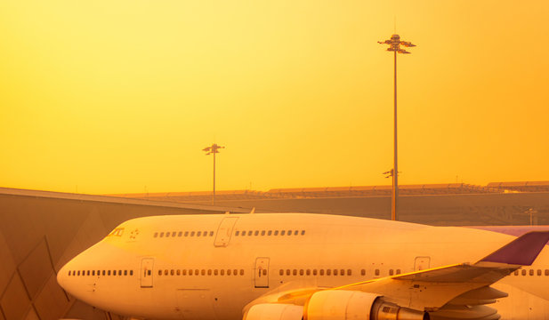 Commercial airplane parked at the airport. Global aviation business crisis from coronavirus. Failed journey vacation flight. Air transportation. Aircraft parked at the airport with orange sunrise sky.